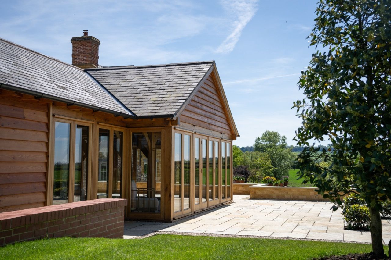 St Dennis Pool House, A large wooden house with a lot of windows and a patio in front of it.
