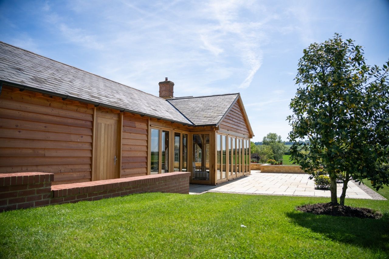 St Dennis Pool House, A large wooden house with a lot of windows is sitting on top of a lush green field.