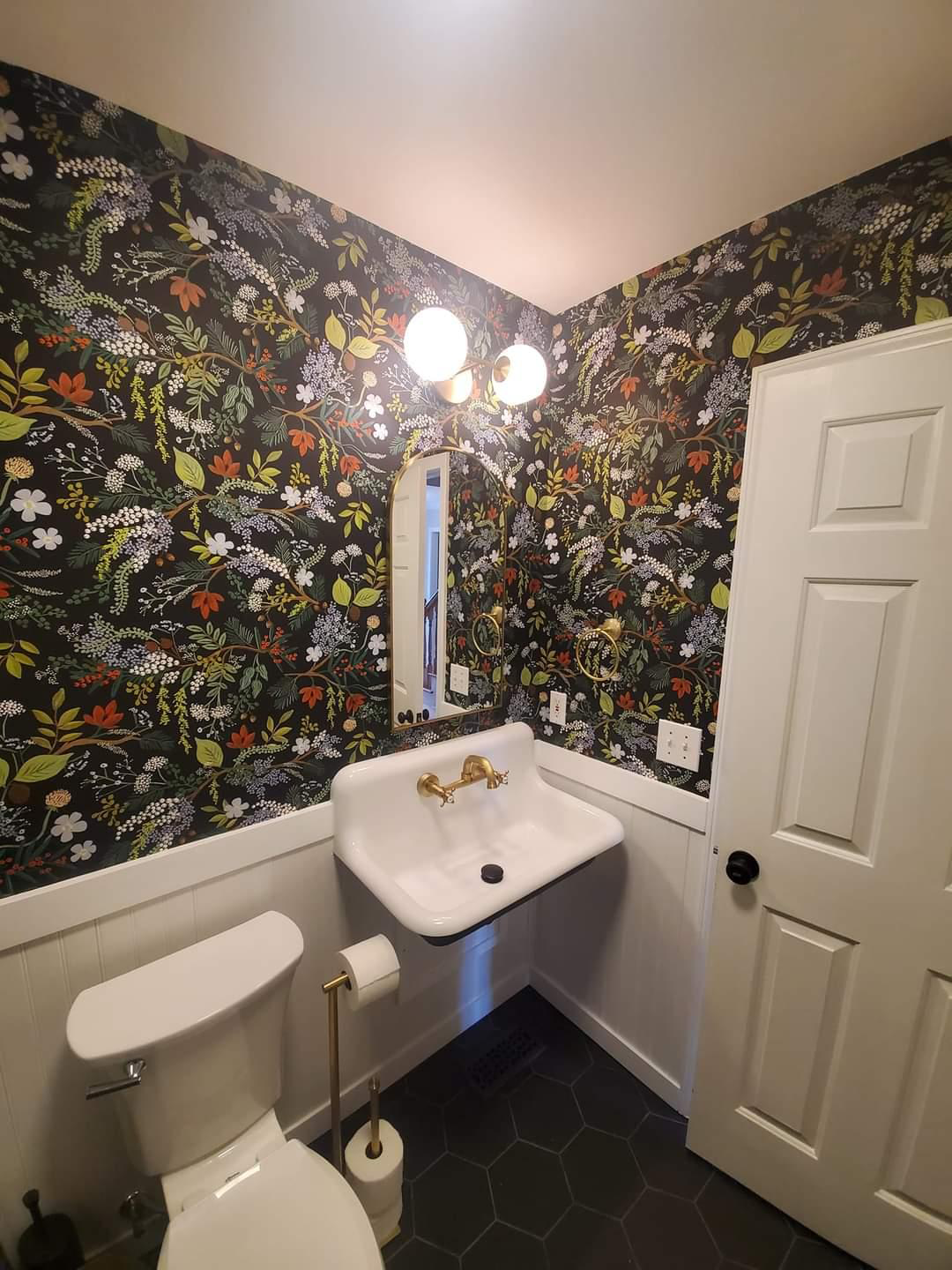 A bathroom with a toilet , sink , mirror and floral wallpaper.