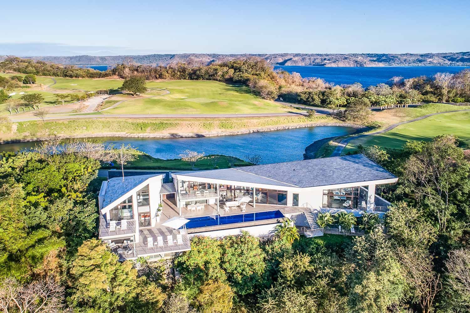 Modern white house with pool, overlooking water and golf course.