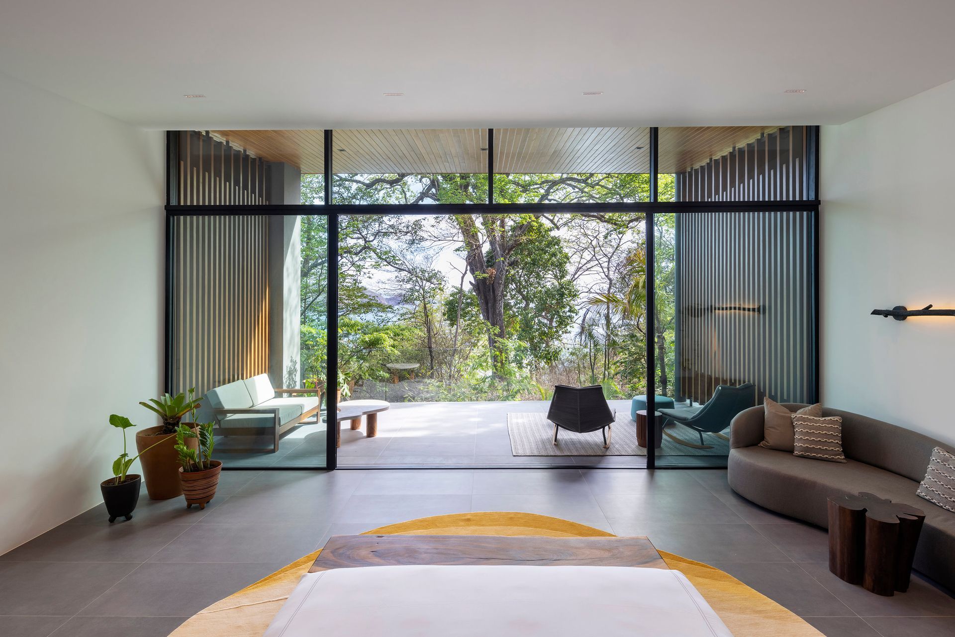 Bedroom with large window overlooking a forest, couches, and a round rug.