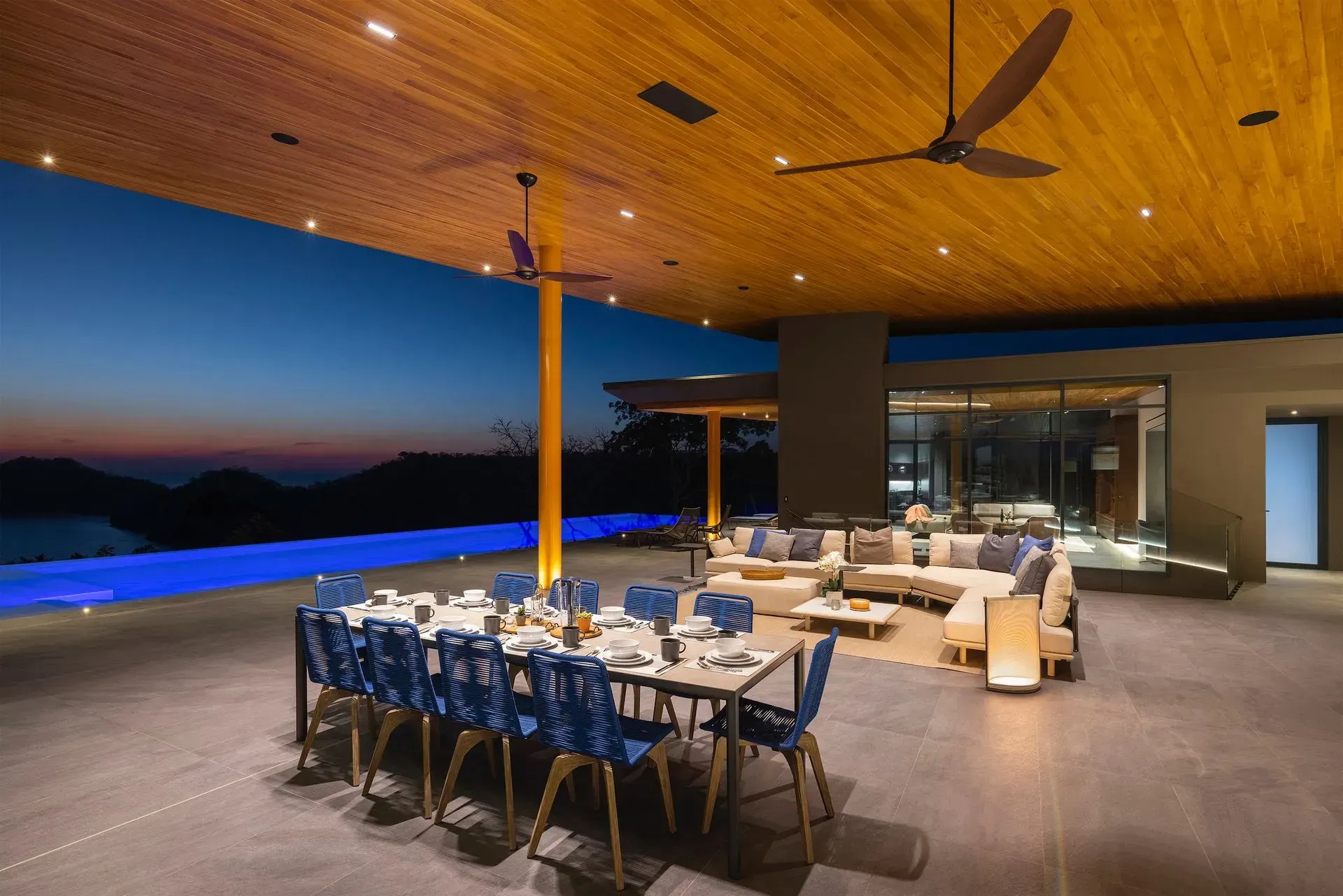 Open-air luxury dining terrace at sunset with a set table, lounge seating, and ocean view