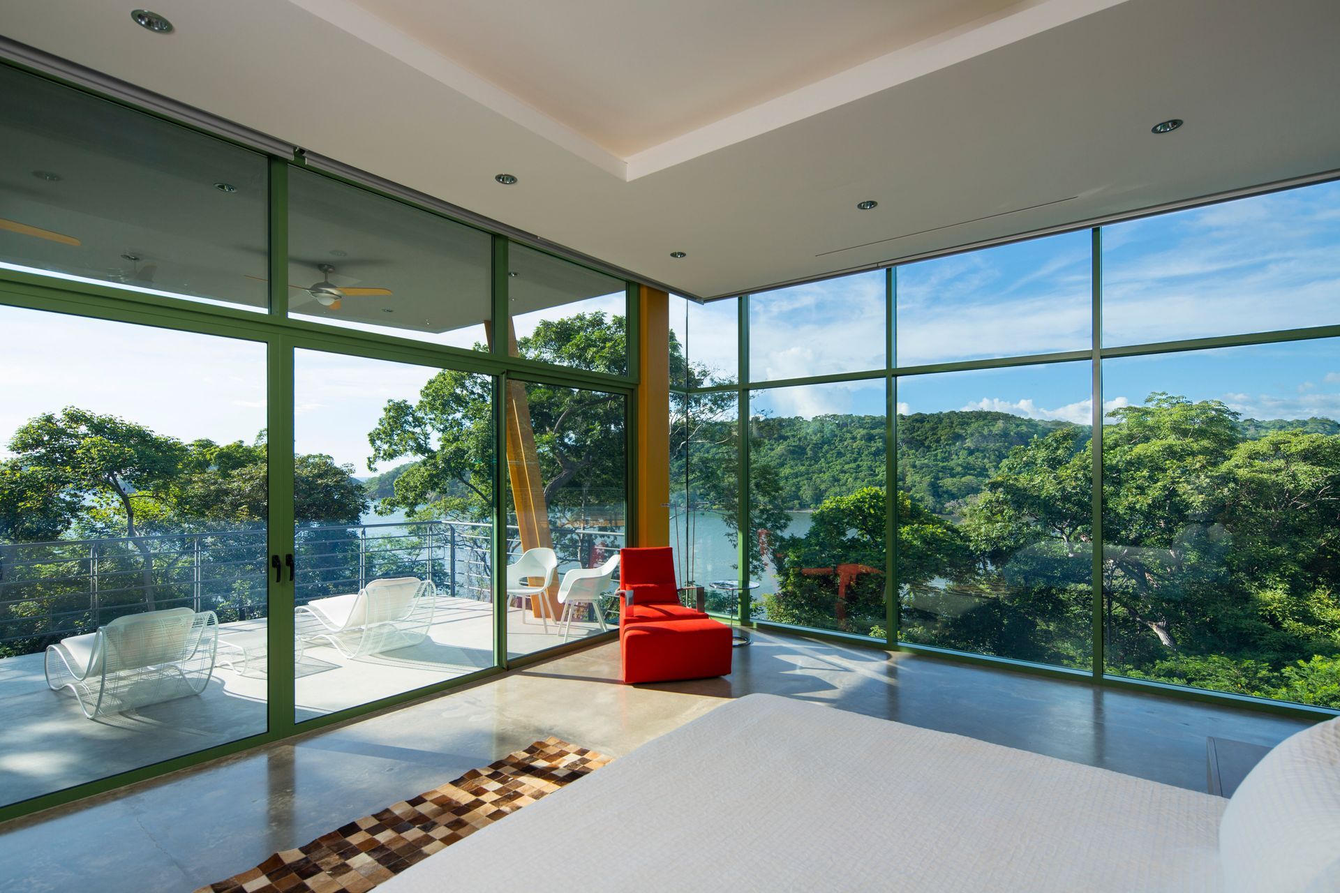Modern bedroom with floor-to-ceiling windows overlooking a lush, green landscape and lake.