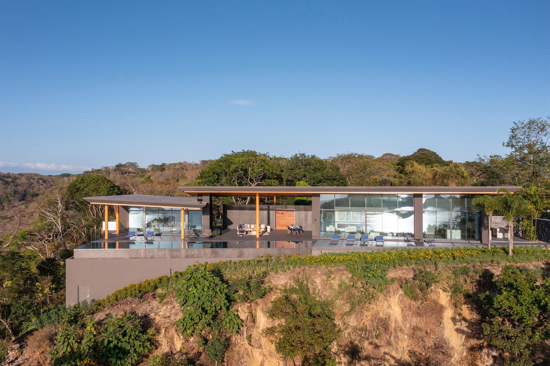 A large house by Sarco Architects is sitting on top of a hill surrounded by trees in the tropics