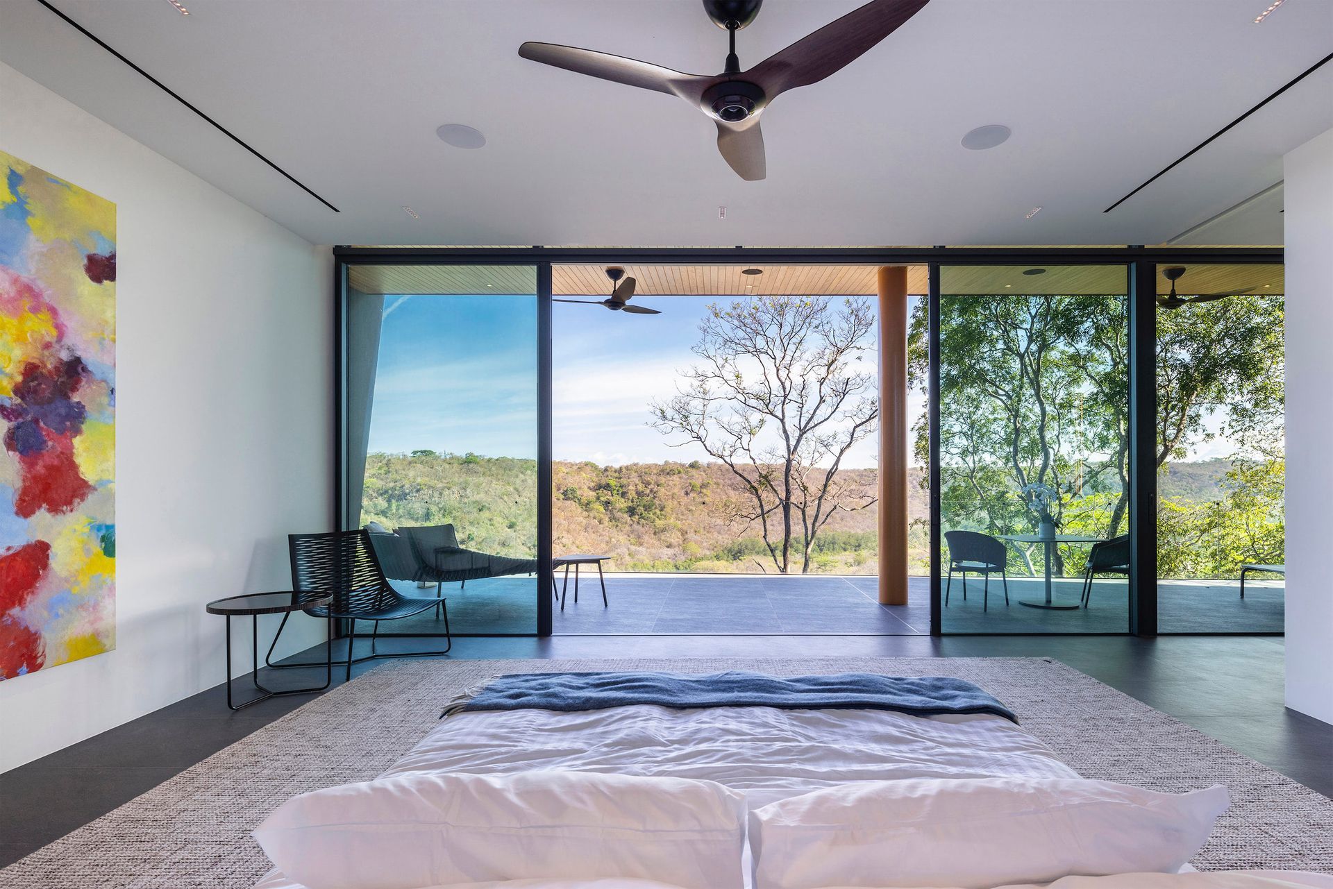 A bedroom with a large bed and a ceiling fan looking over a cliff, showcasing privacy and nature