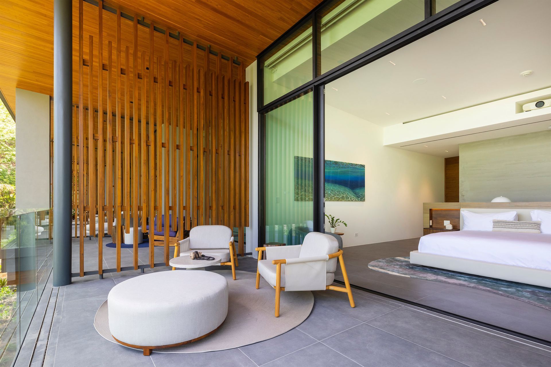 a bedroom with a large bed , chairs , ottoman and sliding glass doors .