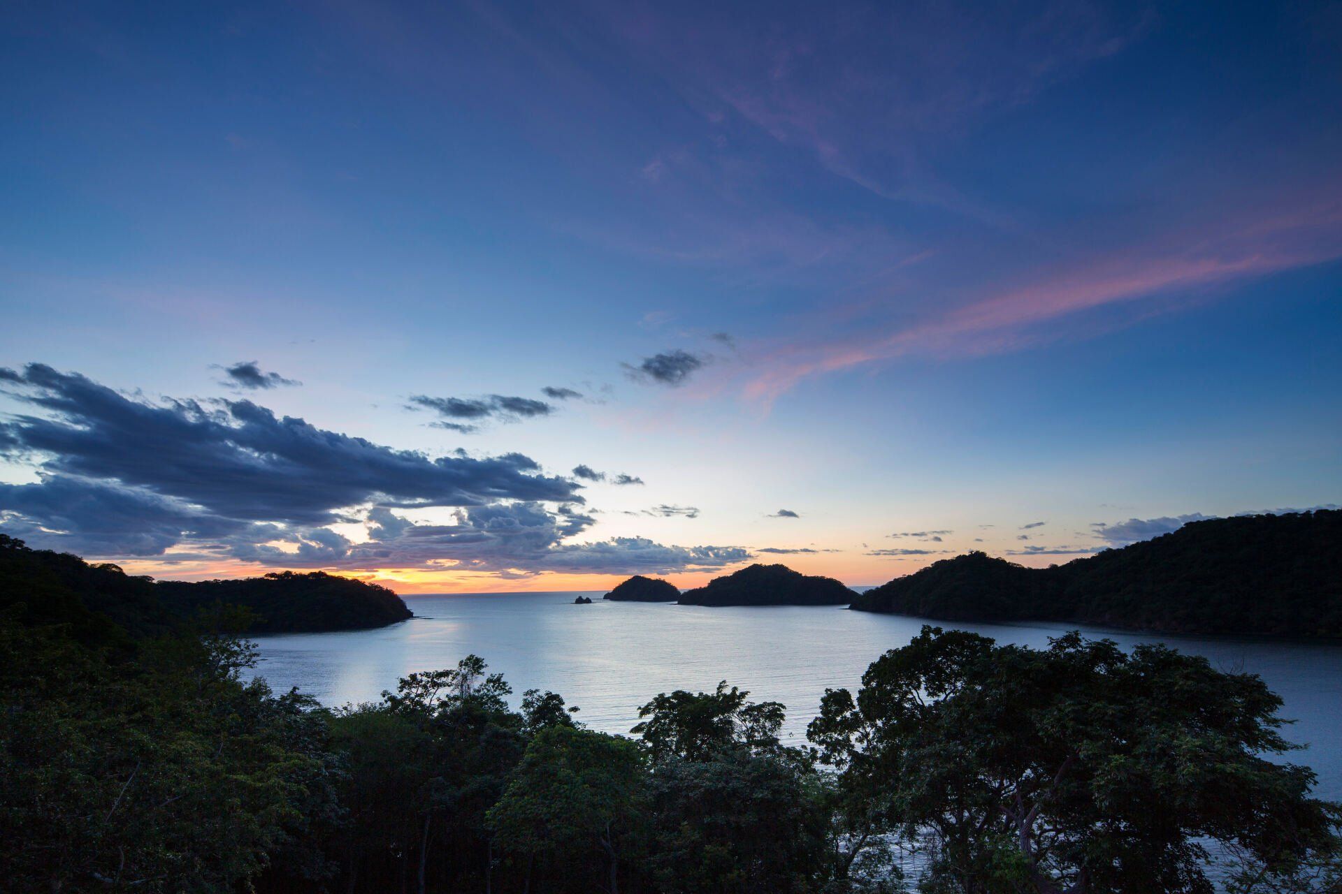 a sunset over a body of water with trees in the foreground