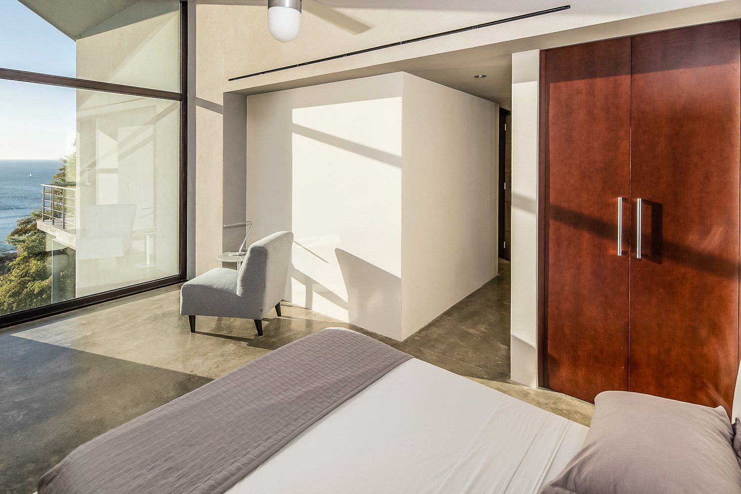 a bedroom with a bed , chair , and large windows overlooking the ocean .