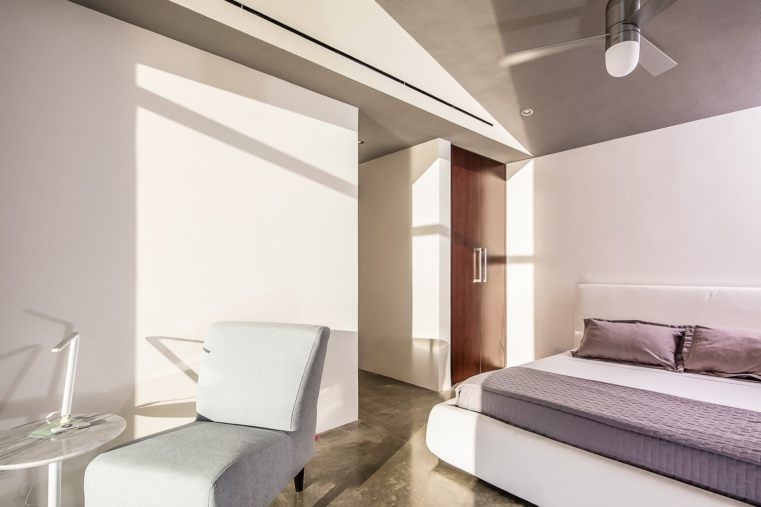 a bedroom with a bed , chair , table and ceiling fan