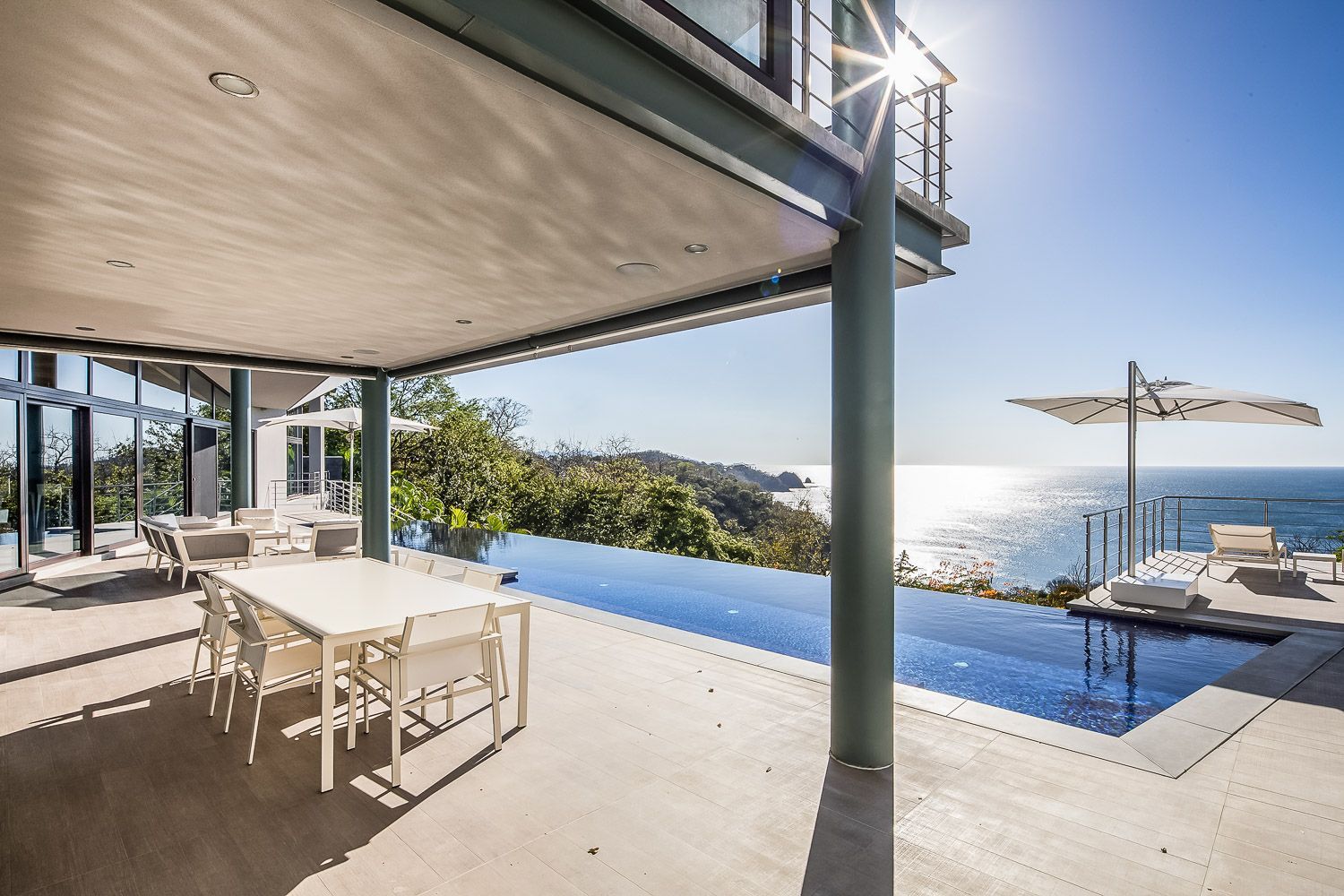 Patio with a pool overlooking the ocean, white furniture, sunny day.