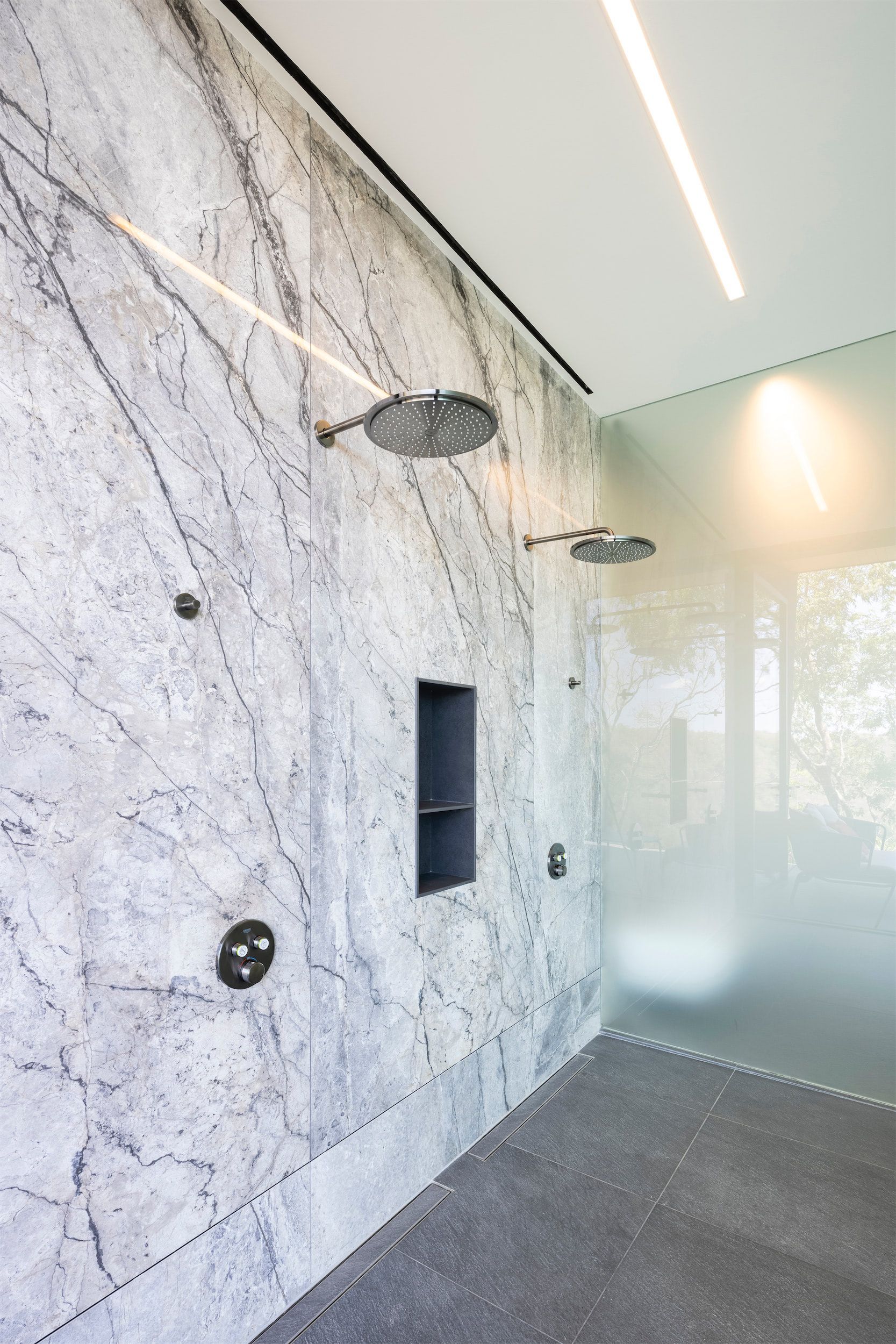 a bathroom with a marble wall and two shower heads .