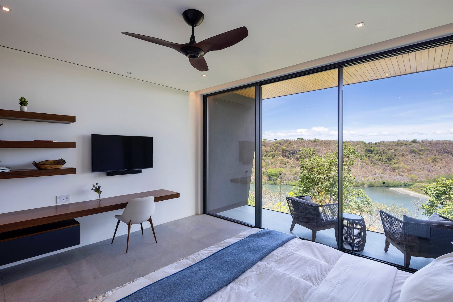 a bedroom with a large bed , desk , television and sliding glass doors .