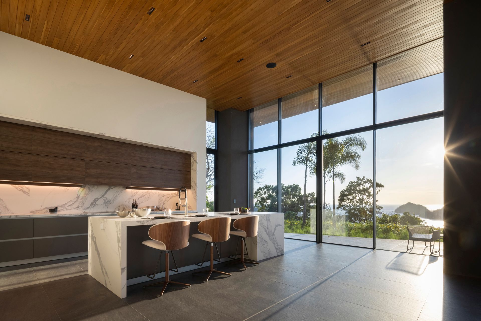 A luxury style kitchen with a large island and panoramic windows looking at the sea