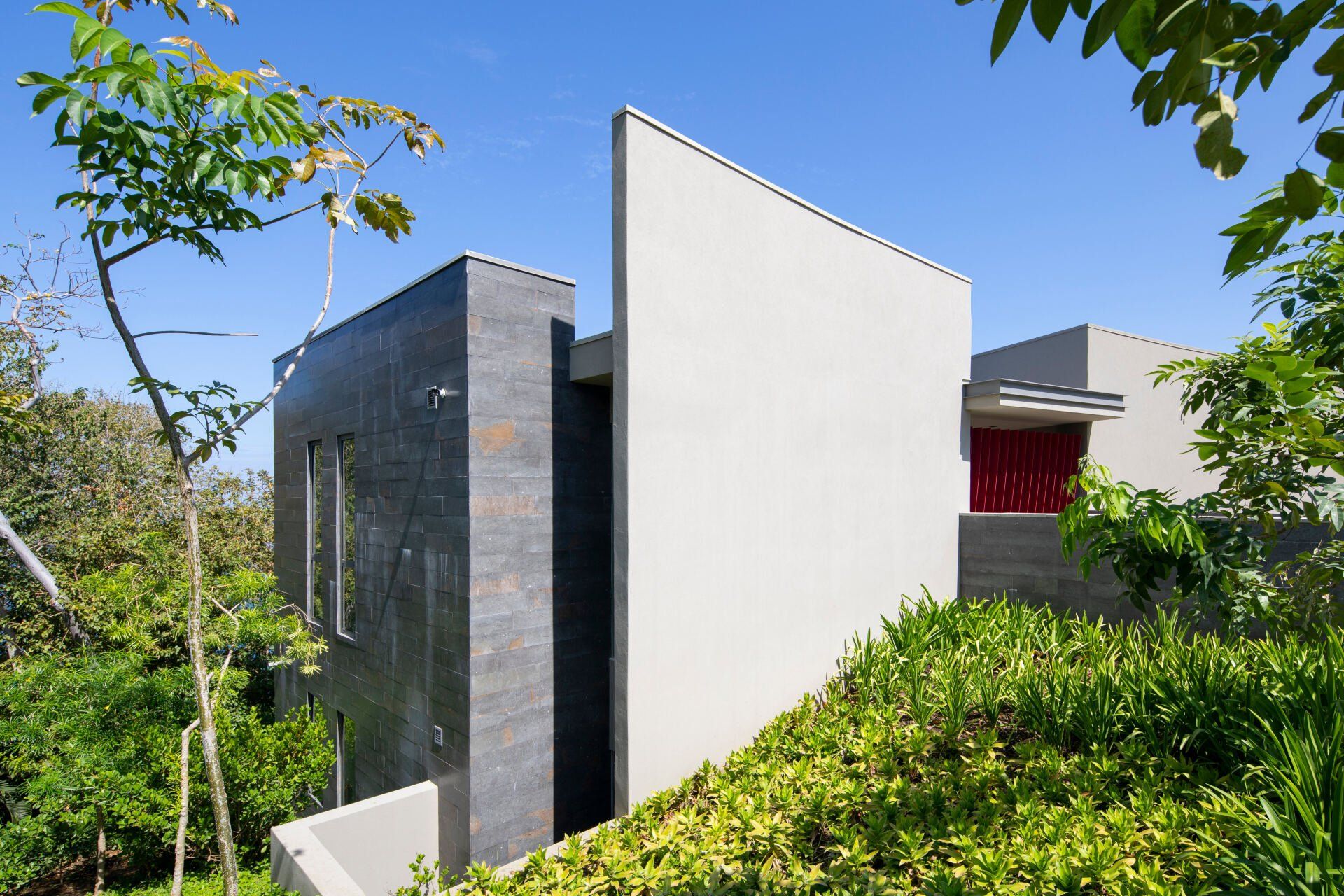 a white building with a red window is surrounded by trees and bushes