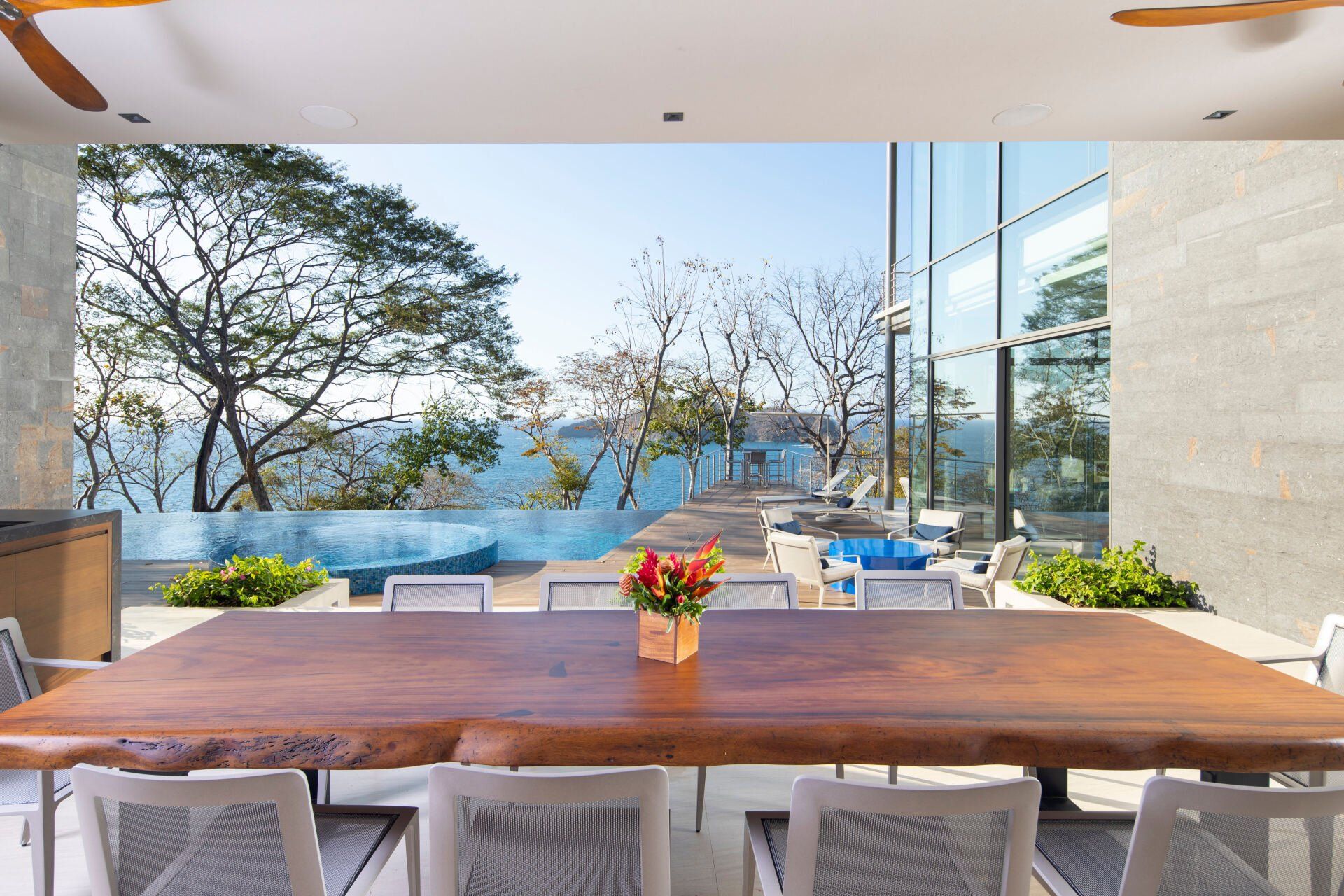 a large wooden table with a vase of flowers on it in a dining room with a view of the ocean .