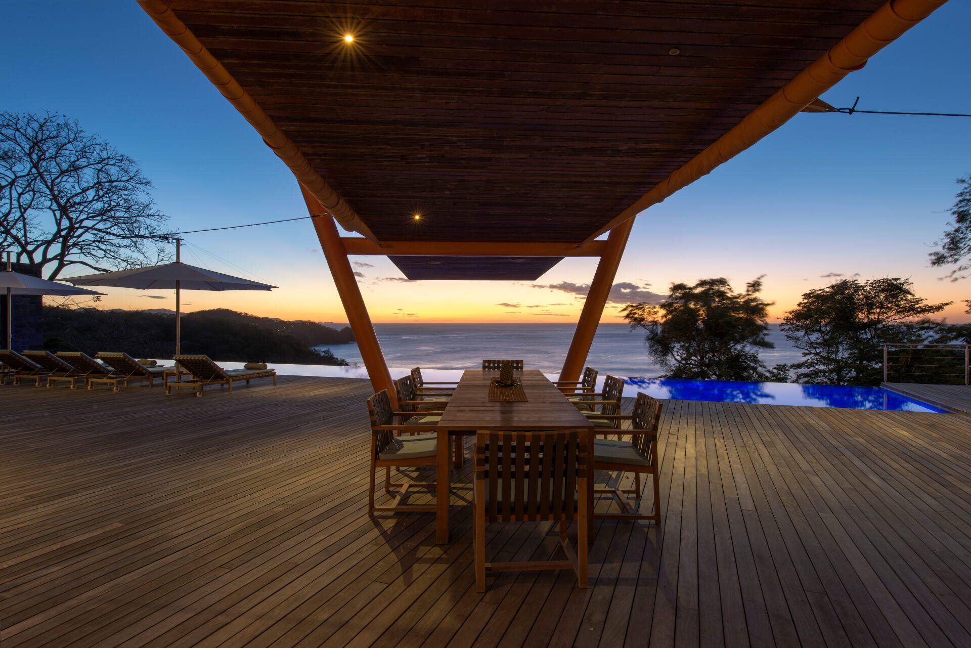 a wooden deck with a table and chairs under a canopy overlooking the ocean
