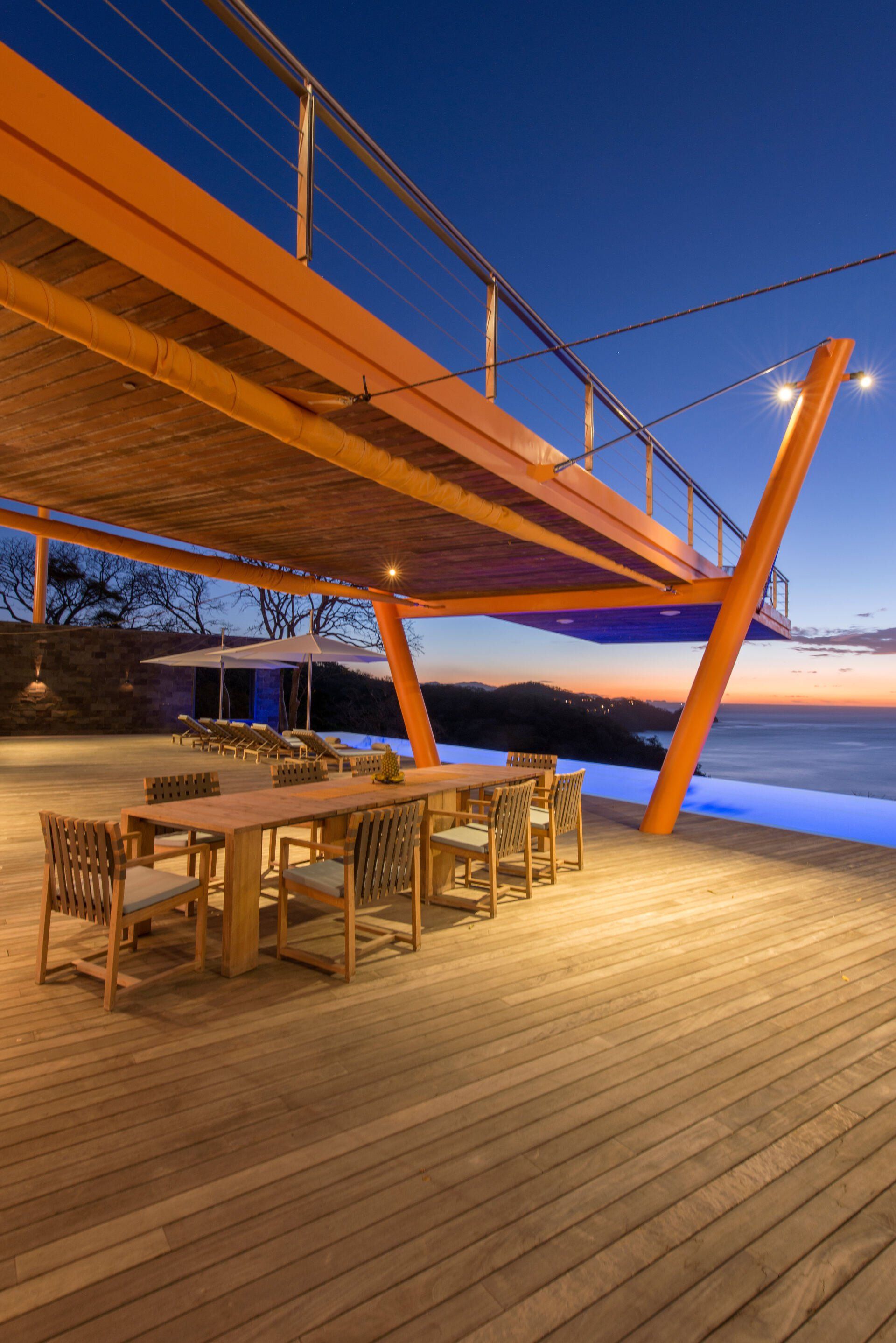 a wooden deck with tables and chairs under a bridge overlooking the ocean .