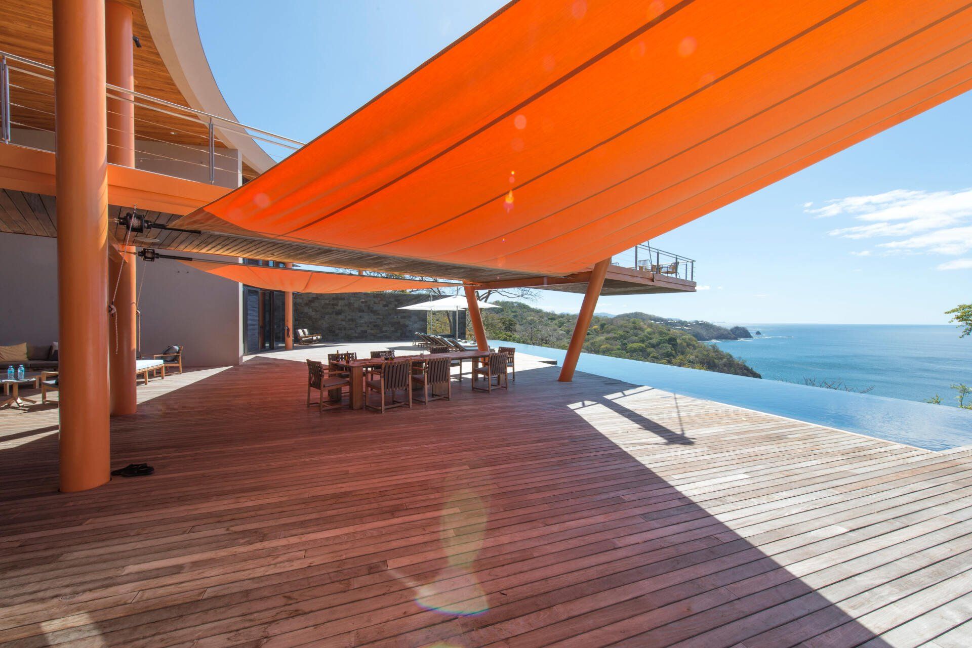 a wooden deck with tables and chairs under an orange umbrella overlooking the ocean .