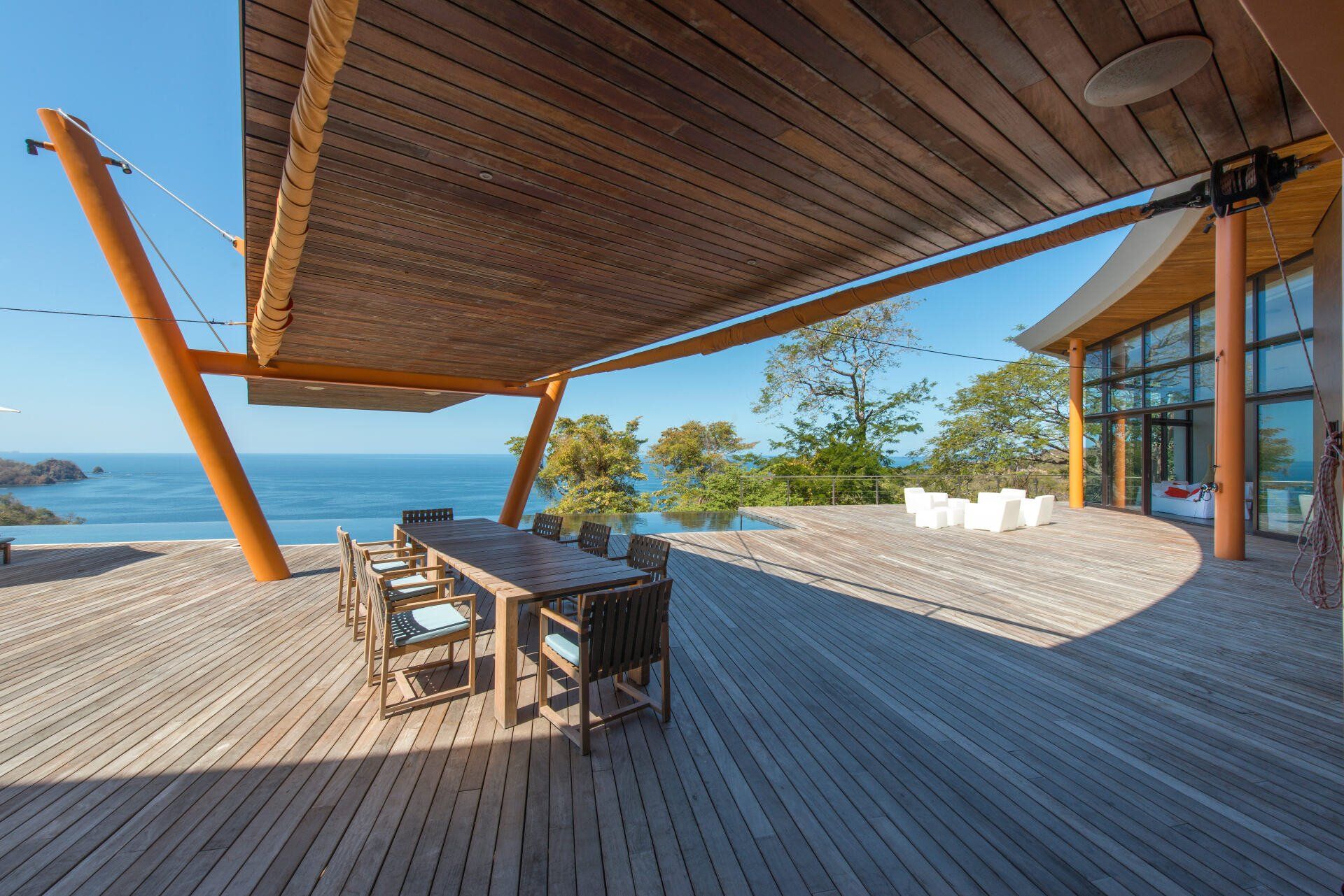 a large wooden deck with a table and chairs under a canopy overlooking the ocean .