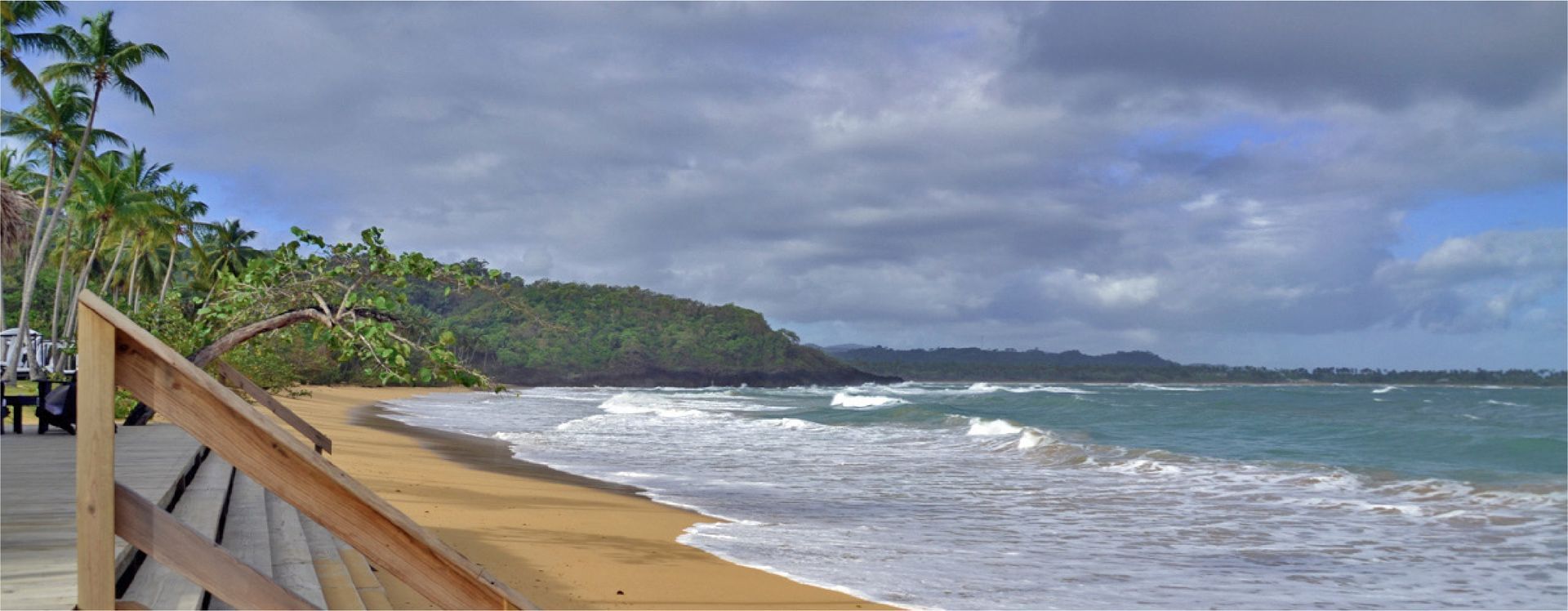 a wooden walkway leading to the ocean on a cloudy day