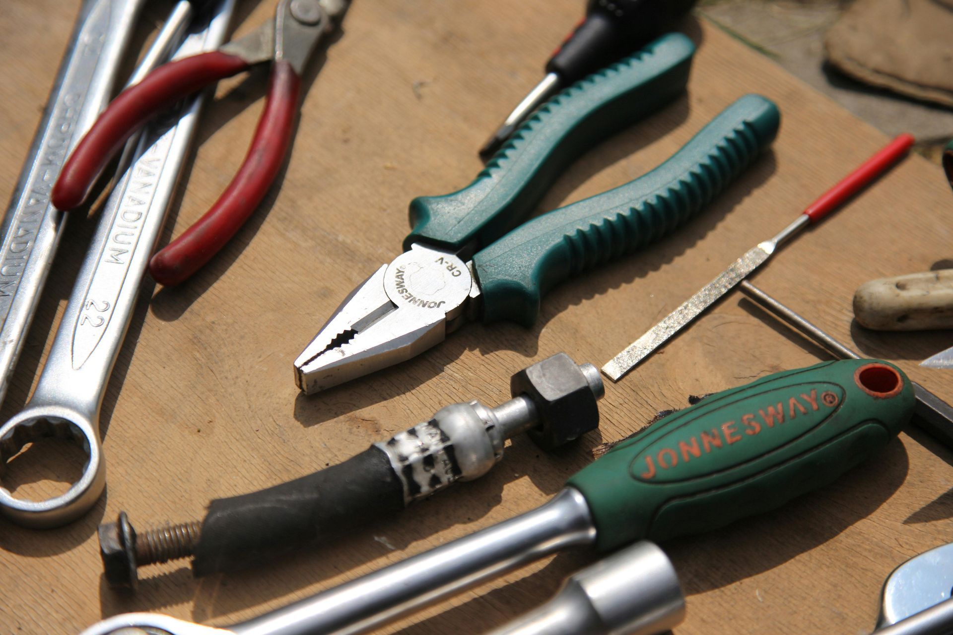 Assorted hand tools on a wooden surface, including pliers, wrench, and screwdriver
