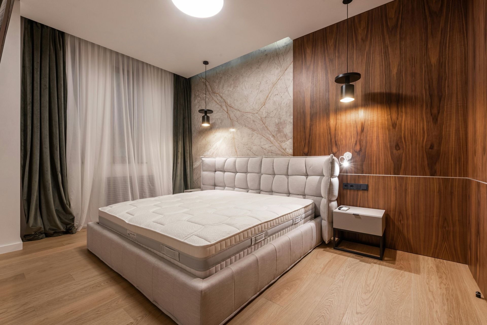 Modern bedroom with a large bed, wood-paneled wall, bedside lamp, and floor-to-ceiling curtains