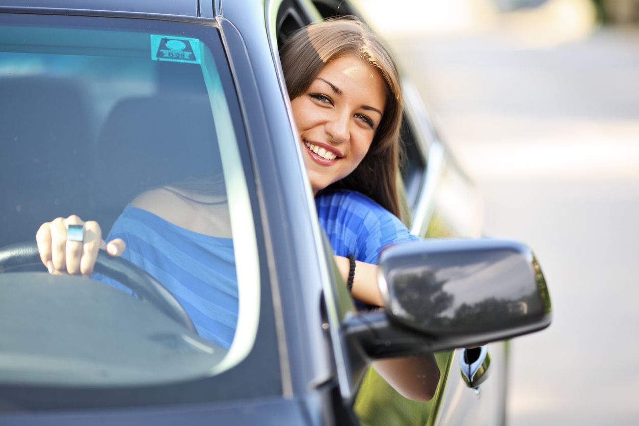 A woman in a blue shirt is driving a car and smiling.