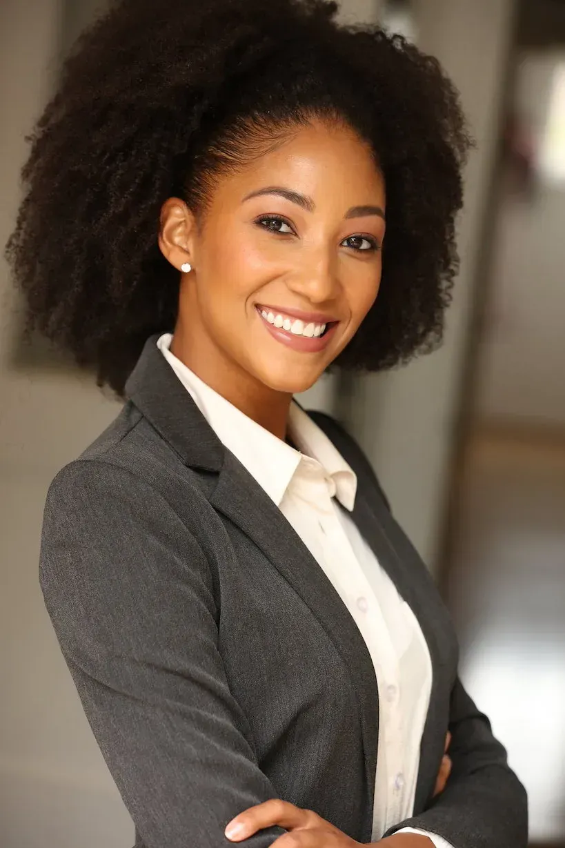 A woman with an afro is wearing a suit and smiling with her arms crossed.