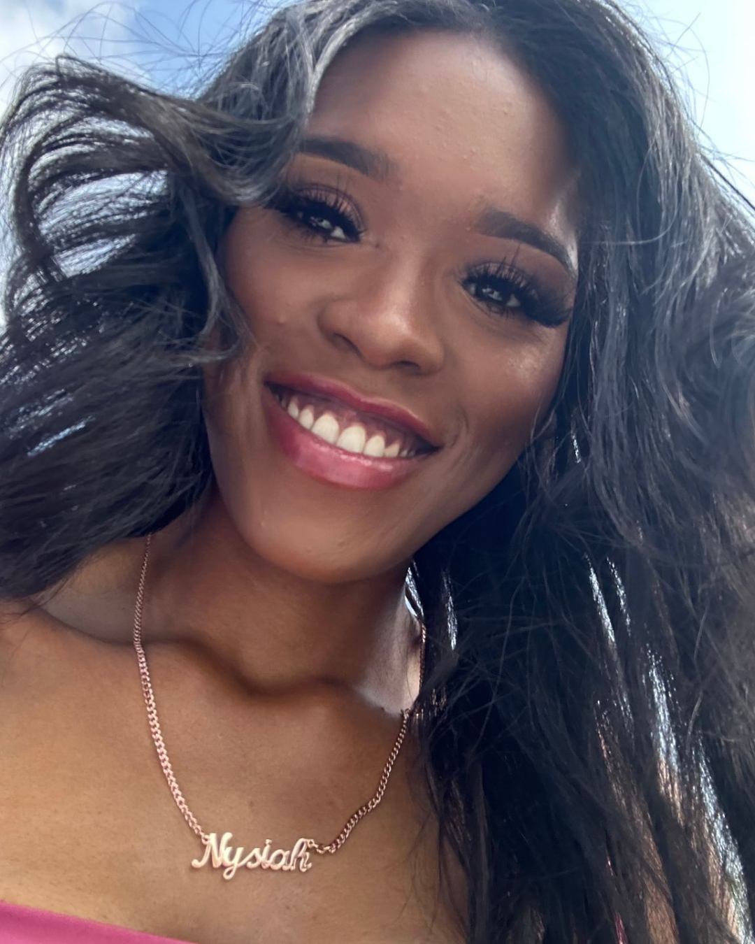 Woman smiling at a table, eating a burger and chips in a restaurant, wearing a sweater.