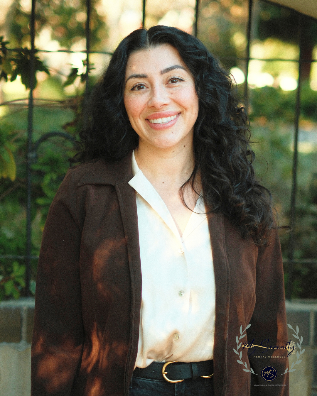 Woman in a blazer and white shirt smiles at the camera, with a fluffy afro.