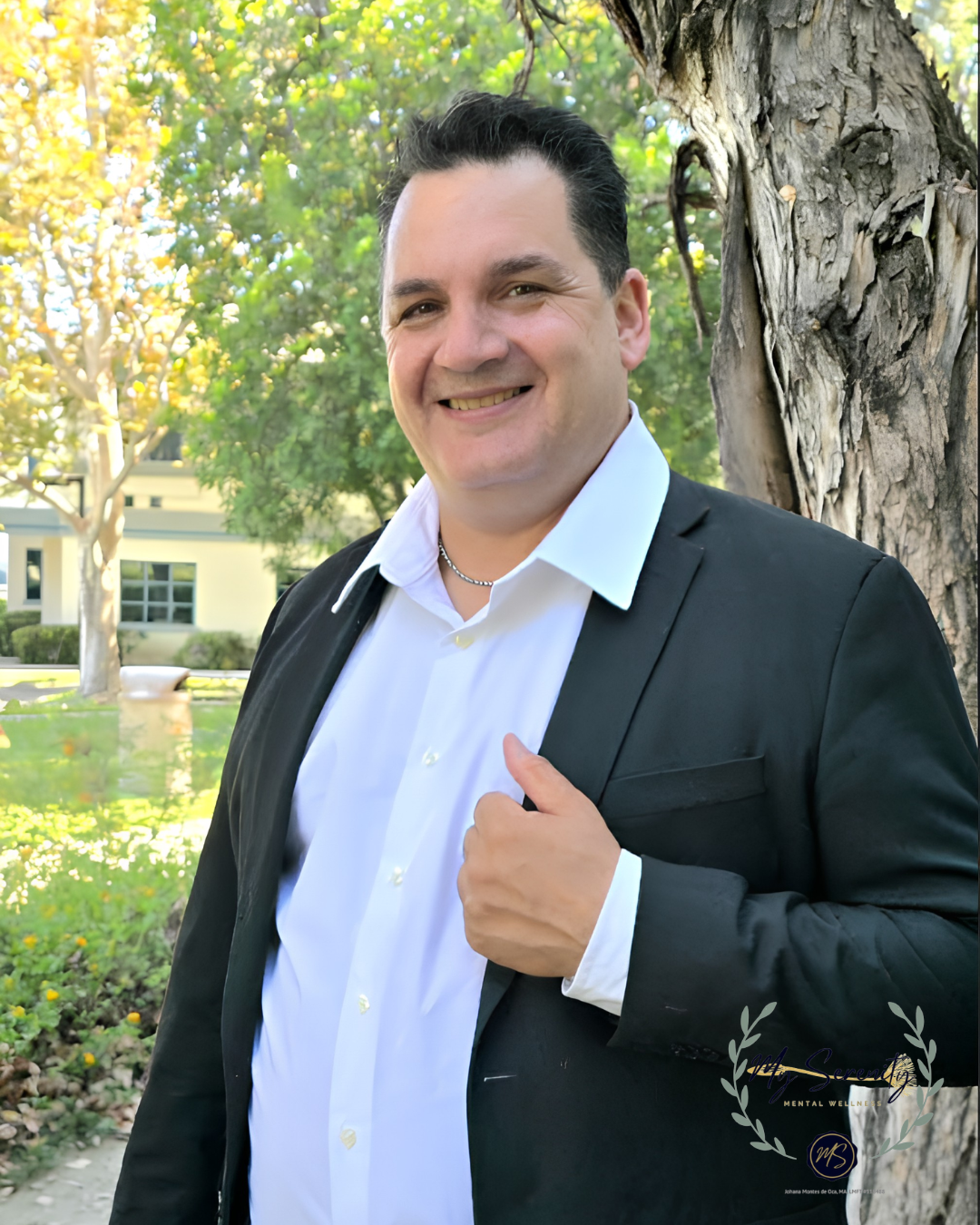 Smiling person in a black top standing outdoors in front of green leaves.