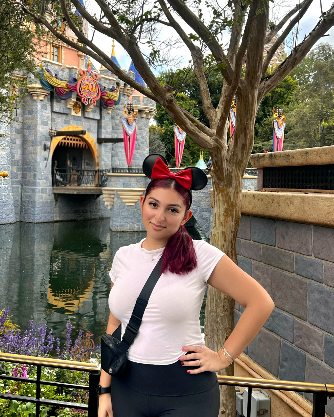 Woman wearing Minnie Mouse ears in front of a castle, posing with hand on hip.
