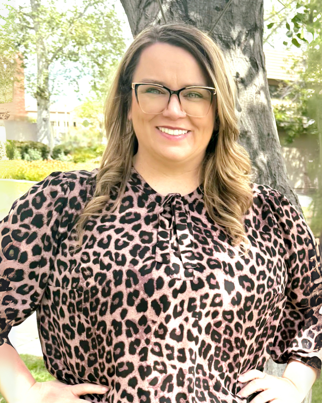 A woman is standing in front of a tree with her hands on her hips.