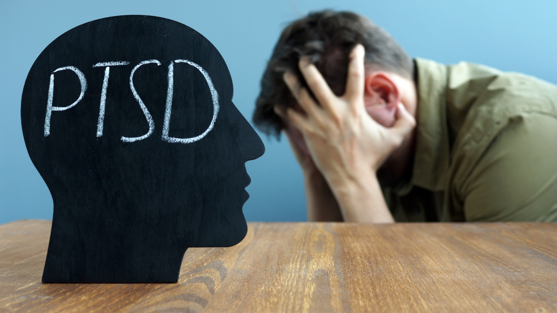 A man is sitting at a table with his head in his hands next to a sign that says ptsd.
