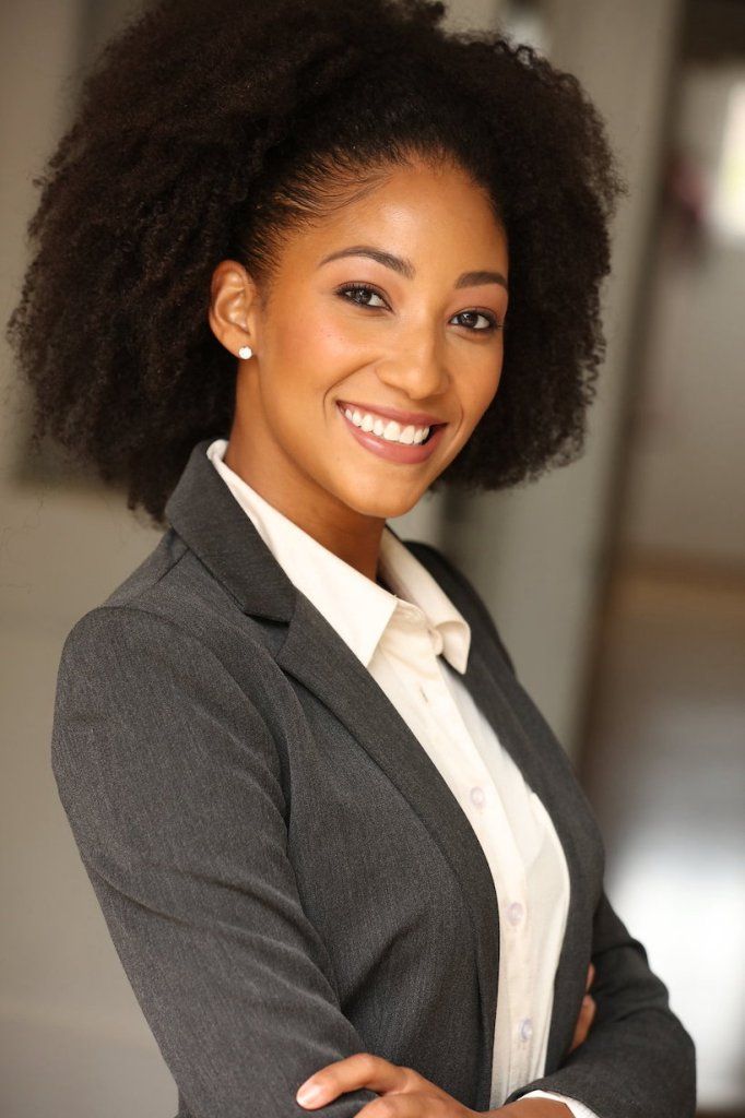 A woman with an afro is wearing a suit and smiling