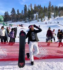 A woman is standing in the snow holding a snowboard.