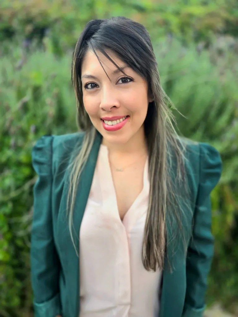 A woman wearing a green jacket and a pink shirt is smiling for the camera.