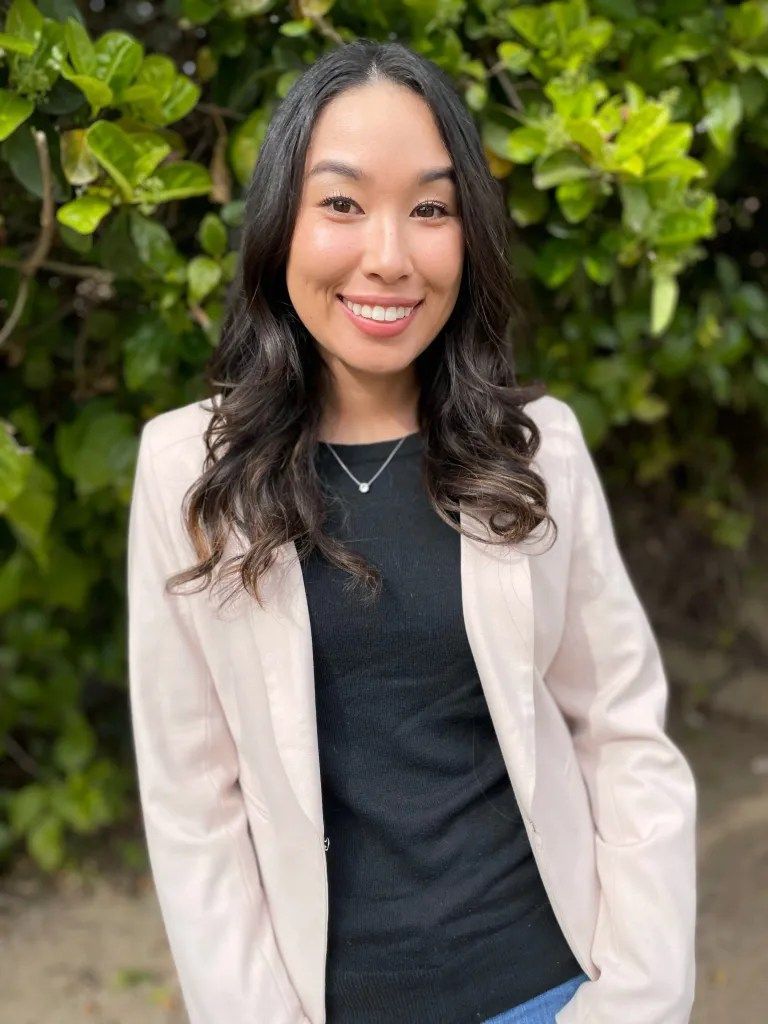 A woman in a pink jacket and black shirt is smiling for the camera.
