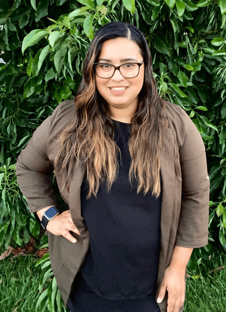 A woman wearing glasses and a watch is standing in front of a tree.