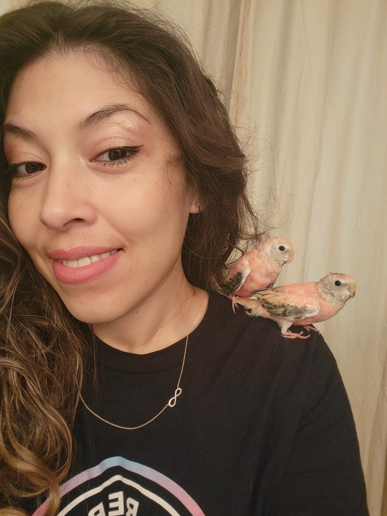 A woman is holding two small birds on her shoulder.