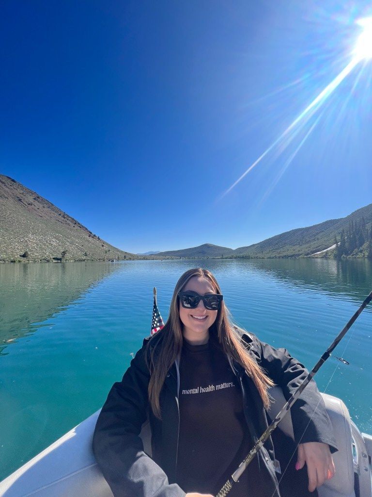 A woman is sitting in a boat on a lake holding a fishing rod.