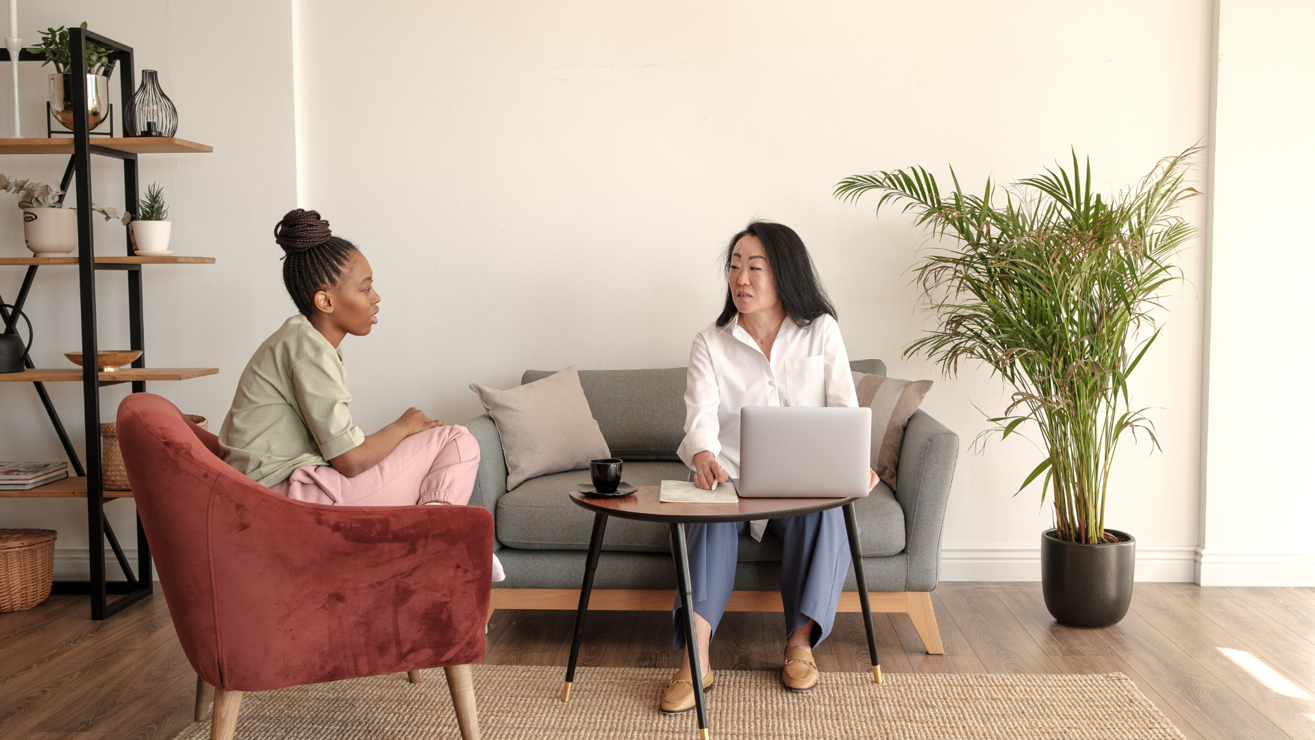 Two women are sitting on a couch talking to each other in a living room.