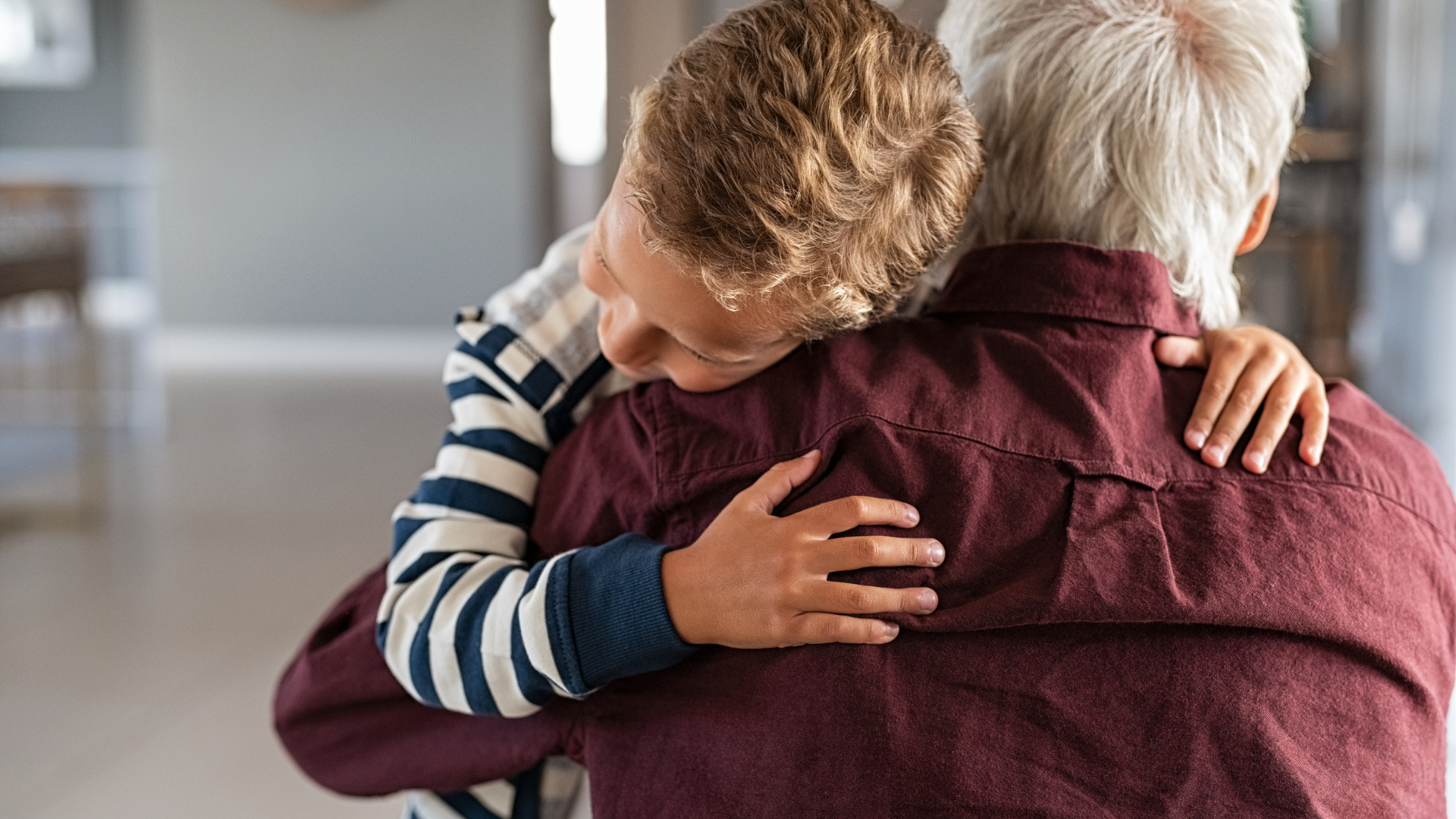 A young boy is hugging an older man in a living room.