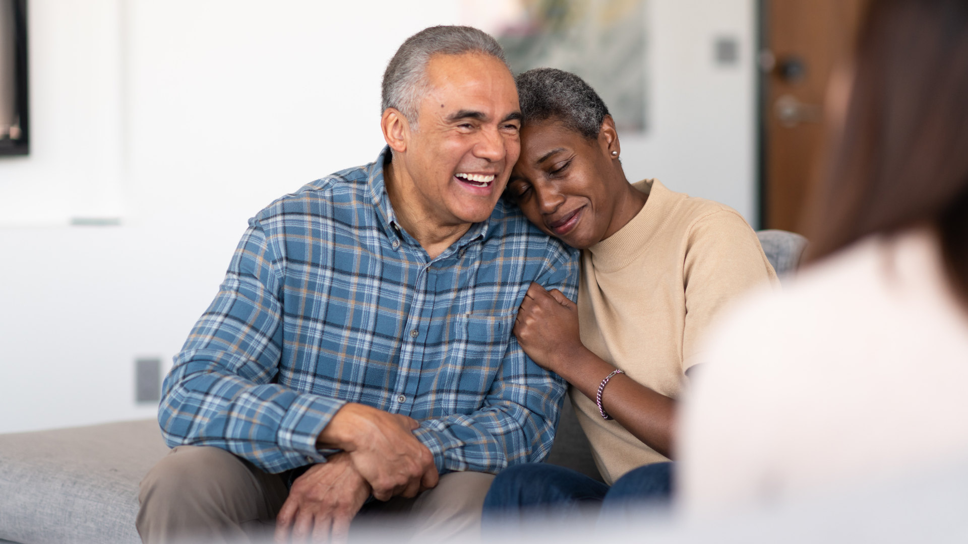 An elderly couple is sitting on a couch talking to a woman.