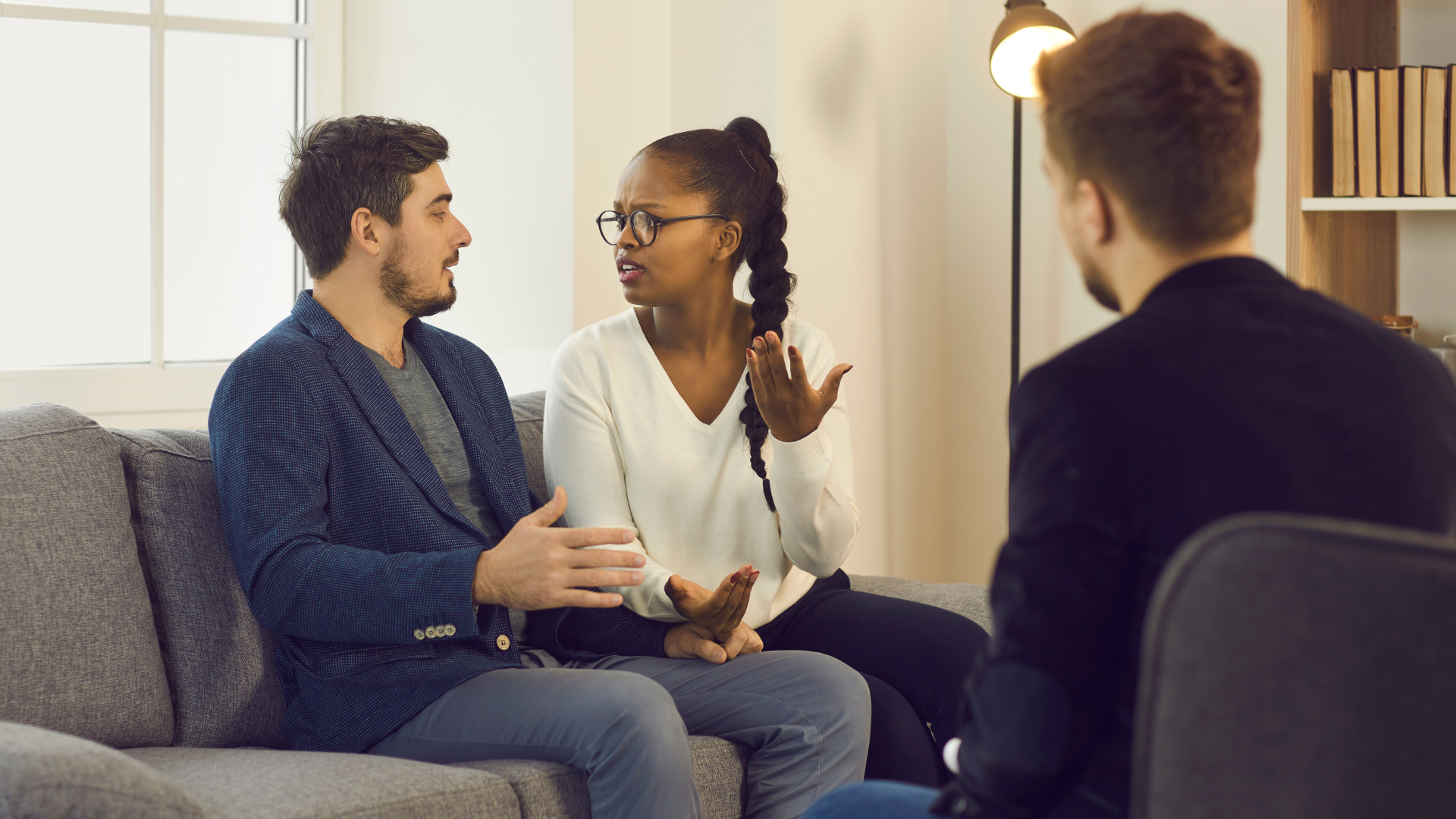 A man and a woman are sitting on a couch talking to a man.