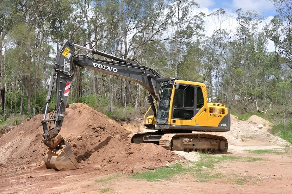 A Yellow Volvo Excavator Is Digging A Hole In A Dirt Field — S & K Raw Materials & Earthmoving in Atherton, QLD