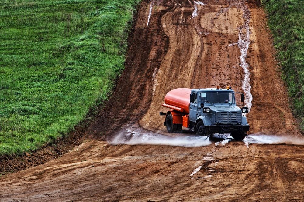 A Tanker Truck Is Driving Down A Dirt Road — S & K Raw Materials & Earthmoving in Atherton, QLD