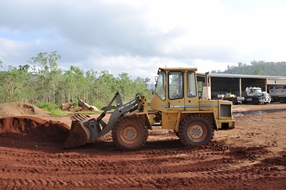 A Yellow Bulldozer Is Moving Dirt In A Field — S & K Raw Materials & Earthmoving in Mareeba, QLD
