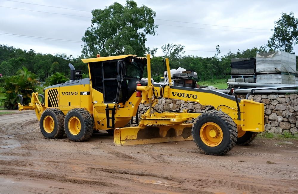A Yellow Volvo Grader Is Parked On A Dirt Road — S & K Raw Materials & Earthmoving in Atherton, QLD
