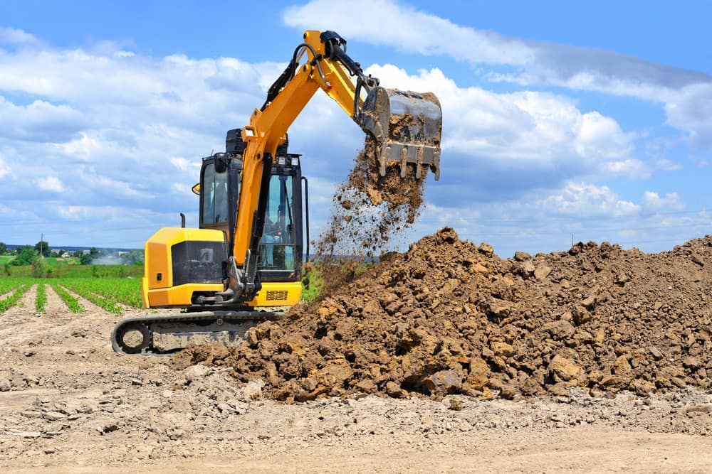 A Yellow Excavator Is Digging A Pile Of Dirt In A Field — S & K Raw Materials & Earthmoving in Atherton, QLD